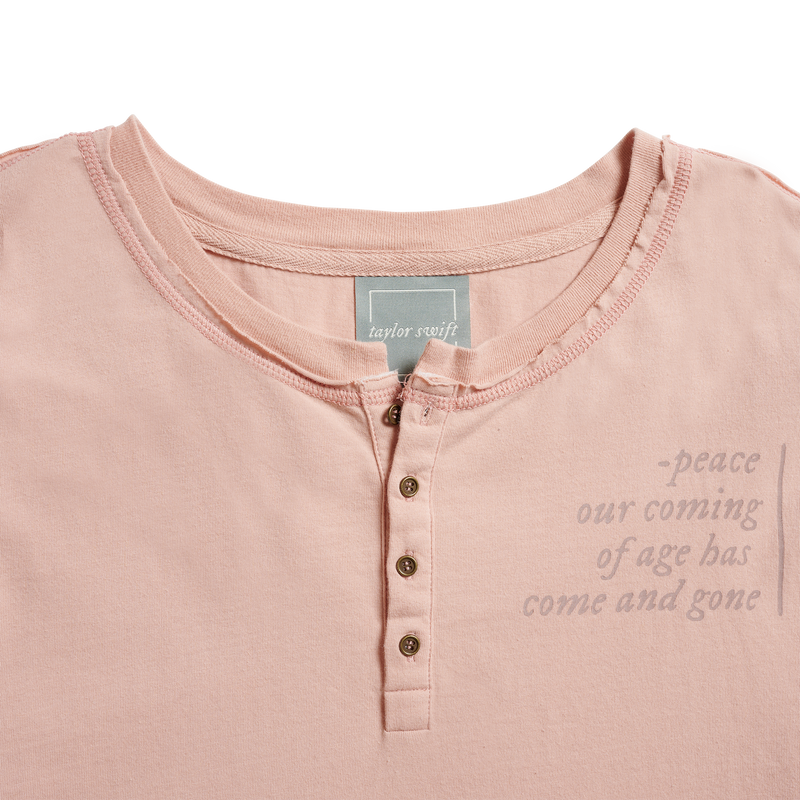 Faded blush long sleeve henley with antique brass buttons, exposed stitching at sides of body, shoulders, and sleeves. Raw edge distressed seams at neck, sleeve cuffs, and hem. Lyrics from the song "peace" printed on left chest, sleeve, and lower back.